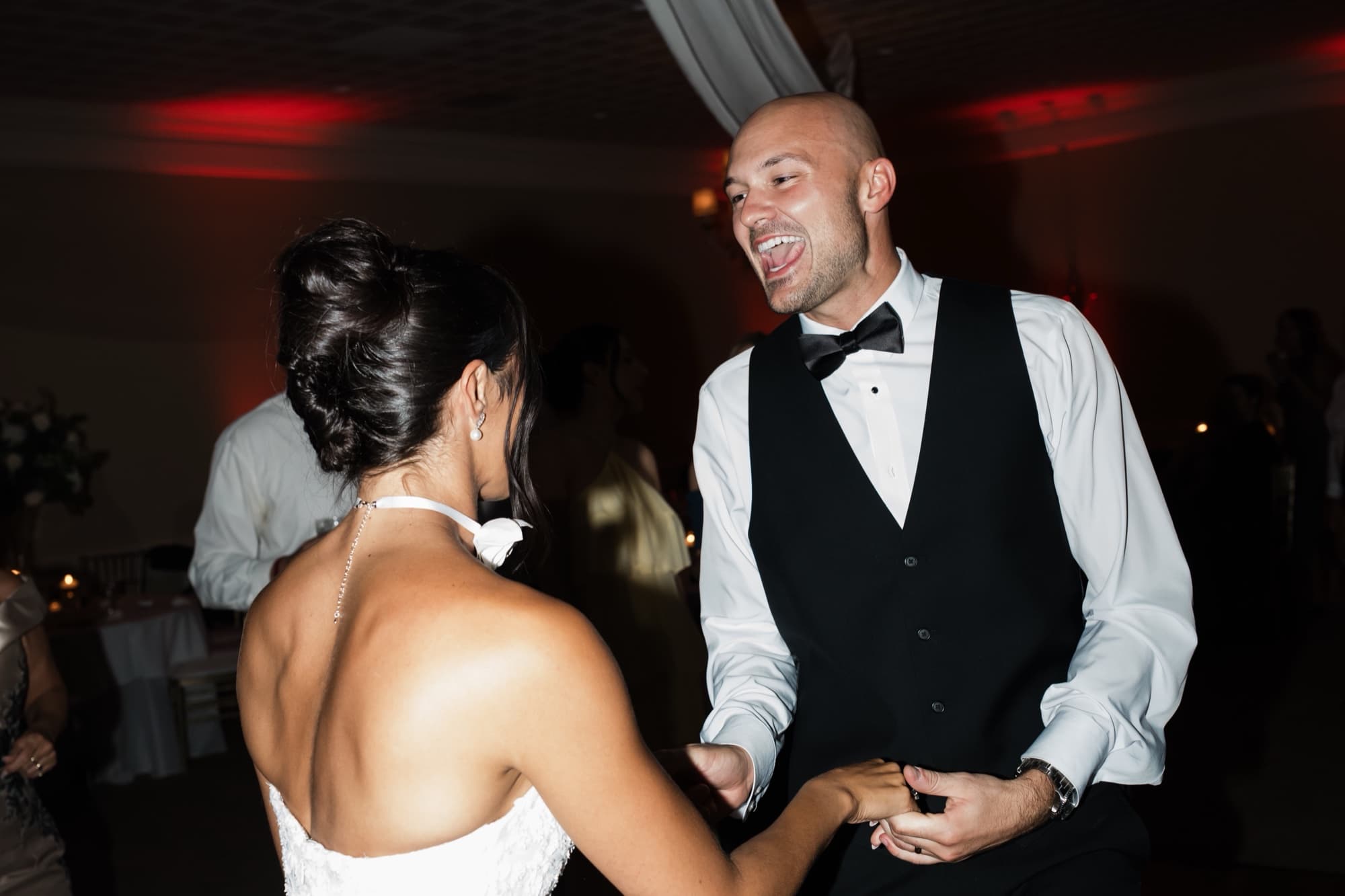 A laughing groom dancing hand in hand with his bride at their wedding reception